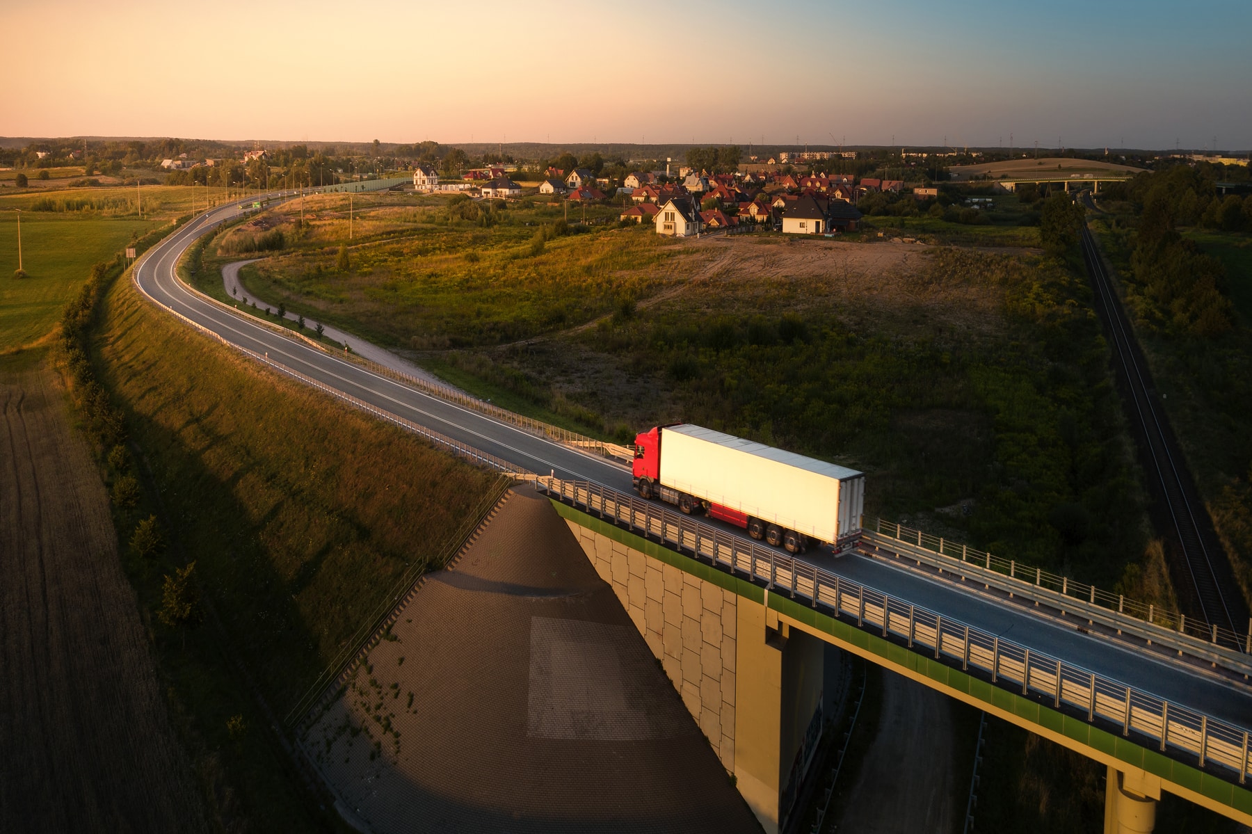 Luftaufnahme eines Lastwagens auf einer Landstraße bei Sonnenuntergang, mit einem Dorf und einer Brücke in einer nordischen Landschaft – sinnbildlich für einen Fuhrpark, der mit erneuerbarem Diesel fährt